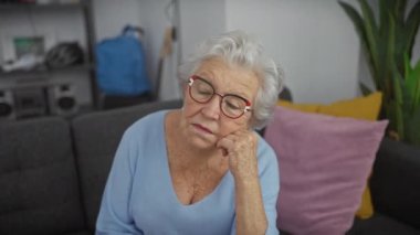 Modern bir oturma odasında koltukta oturan, sükuneti ve tefekkürü yansıtan düşünceli, son sınıf öğrencisi kadın..