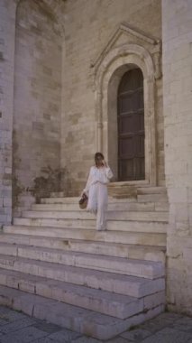 Güzel genç bir kadın, tarihi Puglia caddelerinde antik mimari bir kapı eşiği tarafından çerçevelenmiş şık bir el çantası taşıyan eski bir kasaba olan Bari, İtalya 'nın taş basamaklarından aşağı doğru yürüyor..