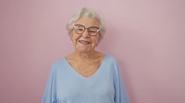 Neşeli, gri saçlı, son sınıf öğrencisi, kendine güvenen, pembe izole edilmiş arka planda neşeli gözlüklü, dişlek bir gülümsemesi olan bir kadın.