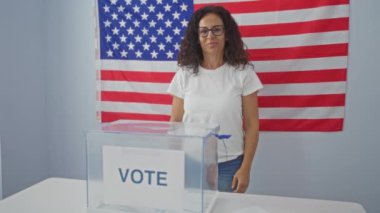 Pozitif değişim için oy verin, mutlu orta yaşlı İspanyol kadın Amerikan seçim koleji oy pusulasının yanında duruyor, onayıyla gülümsüyor.