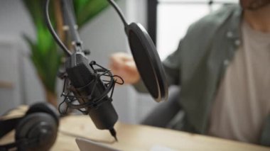 İspanyol adam podcast kaydı için modern radyo stüdyosuna mikrofon yerleştiriyor.