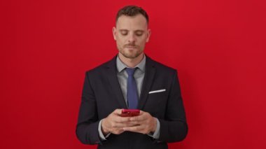 Zeki, takım elbiseli, gülümseyen, kafasını çeviren ve akıllı telefonu kırmızı arka plan üzerinde kullanan genç bir İspanyol.