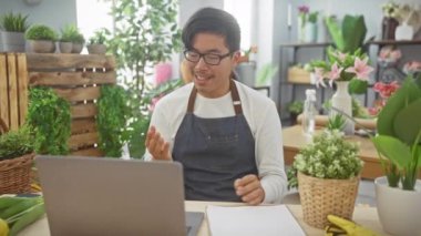Çiçekçi dükkanındaki genç Asyalı bir adam, yemyeşil, bitkiler ve renkli çiçeklerle çevrili bir video konferansına katılmış..