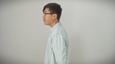 Doğal bir yüzü süsleyen kendine güvenen bir gülümseme, gözlüklü genç Çinli bir adam, rahat bir poz veriyor, basit beyaz izole bir arka plana yan bakıyor.