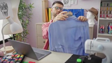 Dikiş makinesi ve modern atölyede kumaşları olan bir gömlek dikmeye odaklanmış bir adam..