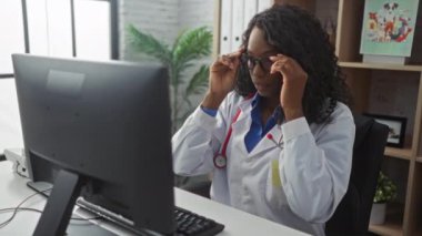 Gözlüklü Afrikalı Amerikalı kadın doktor ve hastane kliniğinde boynunda steteskopla bilgisayar üzerinde çalışıyor..