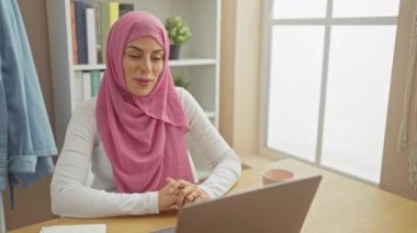 Canlı, tesettürlü, tesettürlü genç bir kadın evinde neşeli bir şekilde gülümsüyor, parmaklarıyla bir gözde 