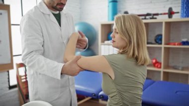 Erkek bir fizyoterapist, kadın bir hastanın kolunu fizyoterapi kliniğinde muayene ediyor..