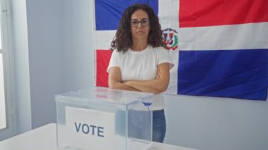 Seçim odasında arkaplanda Dominik Cumhuriyeti bayrağı olan bir seçim sandığının önünde duran kadın.