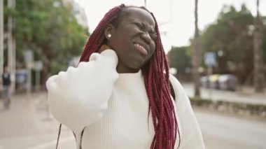 Saçları örgülü Afrikalı bir kadın bir caddede boyun ağrısı çekiyor.