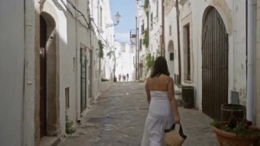 Beyaz elbiseli genç bir İspanyol kadın Puglia, İtalya 'da yaşlı sevimli bir kasaba olan Ostuni' de yürüyor, güneşli bir günde bir sepet taşıyor..