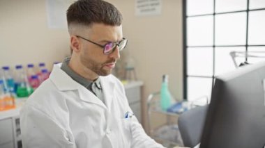 Laboratuvar önlüklü bir İspanyol, parlak bir laboratuvar ortamında bilgisayar ekranındaki verileri analiz ediyor..