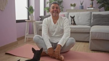 Orta yaşlı bir adam sıcak bir oturma odasında iki chihuahuasıyla yoga yapıyor..