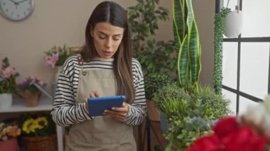 Kapalı alandaki bitkilerin arasında tablet kullanan odaklanmış bir kadın huzurlu bir ev ortamı yaratıyor.
