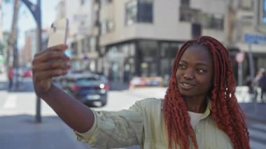 Genç Afrikalı Amerikalı kadın şehir caddesinde akıllı telefonuyla selfie çekiyor..