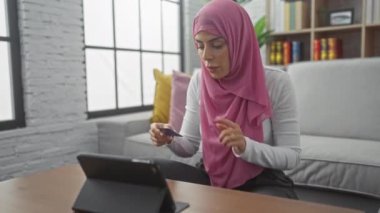 Modern bir oturma odasındaki video görüşmesi sırasında elinde kredi kartı olan tesettürlü genç, İspanyol bir kadın endişeli görünüyor..