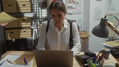 Karmaşık bir polis ofisinde dizüstü bilgisayarı üzerinde çalışan bir kadın dedektif. Rozetli bir adam ise belgeleri inceliyor..