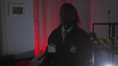 Ciddi bir Afro-Amerikalı kadın dedektif loş ışıkta duran bir suç mahallinde duruyor, otoriteyle kollarını kavuşturuyor..