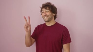 Genç, gülümseyen İspanyol adam cazibesini kırıyor, göz kırpıyor ve zafer kazananın yüzünü parlıyor. Sadece o, sakalı, pembe izole edilmiş bir arka planda tişört giymiş..