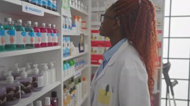 Afrika kökenli Amerikalı kadın eczacı modern bir eczane içinde ürünleri değerlendiriyor.