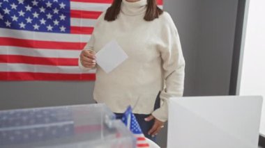 Bir kadın arka planda Amerikan bayrağı olan, demokrasi ve vatandaşlık görevini somutlaştıran bir seçim merkezinde oy kullanıyor..