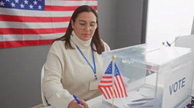 Orta yaşlı bir kadın Amerikan bayrağı ve oy sandığıyla ABD oy kullanma merkezini yönetiyor..
