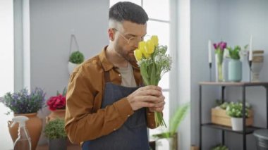 Çiçekçide sarı laleler tutan sakallı yakışıklı İspanyol bir adam. Etrafı yemyeşil çiçeklerle çevrili..