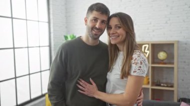 Gülümseyen bir erkek ve kadın romantik bir şekilde sıcak, aydınlık bir oturma odasında kucaklaşıyorlar, evde sevgi dolu bir ilişki olduğunu ima ediyorlar..