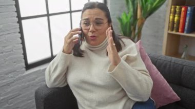 İspanyol bir kadın oturma odasında telefonla konuşuyor. Moda bir iç mekan ile duygularını ve jestlerini sergiliyor..