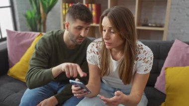 Çift, modern bir oturma odasında rahat bir koltukta akıllı telefonla iletişim, teknoloji ve ev hayatı temalarını çağrıştırıyor..