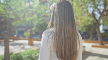 Sakin bir şehir parkında düşünceli bir kadın yeşil ağaçların ve modern şehir mimarisinin ortasında güneşli bir günün tadını çıkarıyor..