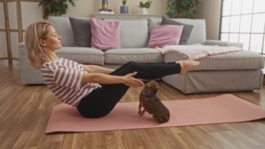 Sarışın genç bir kadın, sıcak bir oturma odasında yoga minderinde chihuahua 'sıyla egzersiz yapıyor..