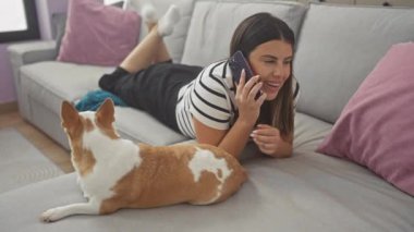 Oturma odasındaki kanepede uzanmış, Chihuahua köpeği eşliğinde genç bir kadın telefonda konuşuyor..
