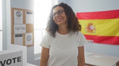 İspanyol seçim kolejinde duran bir kadın. Orta yaşlı, kendine güvenen bir gülümsemesi olan, başka tarafa bakan ve oy verirken gülen bir İspanyol.