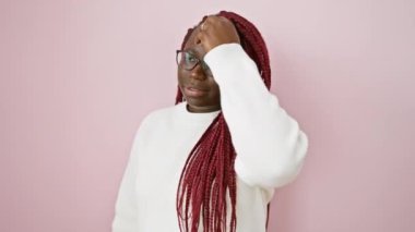 Örgülü ve gözlüklü güzel bir kadın pembe bir arka planda poz veriyor, kendine güveni ve tarzı var..