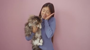 Genç Çinli kadın ve kedi birlikte başarıyı kutlarken mutlu bir ifadeyle, izole edilmiş pembe arka planda neşeyle gülümsüyorlar.