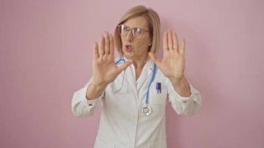 Pembe arka planda steteskoplu beyaz önlüklü orta yaşlı kadın doktor..