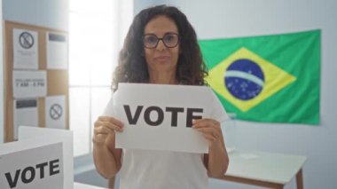 Orta yaşlı İspanyol kadın elinde gururla oy kağıdı tutuyor. Brezilya seçim okulunda zafer ve başarı için heyecanlı.