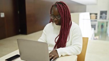 Modern ofis içinde dizüstü bilgisayarla çalışan örgü ören odaklı Afrikalı kadın..