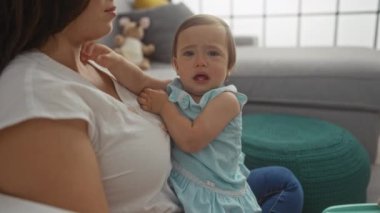 Anne, evdeki modern oturma odasında ağlayan küçük kızı teselli ediyor.