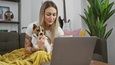 Genç sarışın kadın evde dizüstü bilgisayar ve dekorla köpeğe sarılıyor..