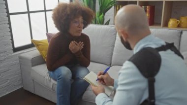 Endişeli bir kadın, kapalı bir ortamda notlar alan odaklanmış bir adamla konuşur, danışmanlık ya da terapi sahnesi yaratır..