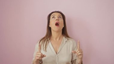 Şaşırtıcı bir şekilde tişörtlü İspanyol bir kadın, pembe arka planda, kendine güvenen bir jest ve neşeli bir şekilde dikiliyor.