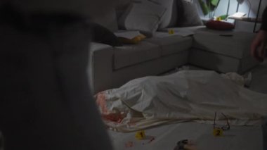 Dedektifler gibi giyinmiş bir kadın ve erkek, kapalı bir suç mahallindeki ipuçlarını dikkatle ve ciddiyetle inceler..