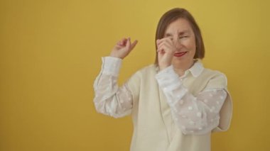 Orta yaşlı İspanyol bir kadın, kameraya doğru bakıyor ve gülümsüyor. İzole edilmiş sarı bir arka planda, hevesle iki eliyle kenarı işaret ediyor.