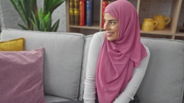 Gülen ve kendinden emin İspanyol bir kadın, neşeli bir gülümseme takınıyor, evinde, rahat bir kanepede kendini kaybetmiş..