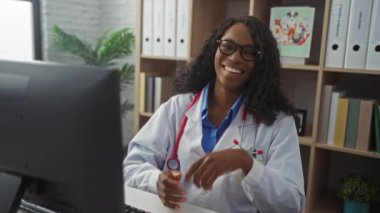 Hastane kliniğinde gözlüğünü çıkarırken kıvırcık saçlı, gülümseyen genç Afrikalı Amerikalı kadın doktor.