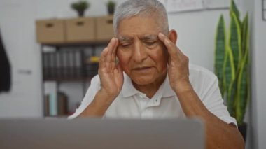 Gri saçlı ve gözlüklü yaşlı bir İspanyol, ofiste otururken stres belirtileri gösteriyor..