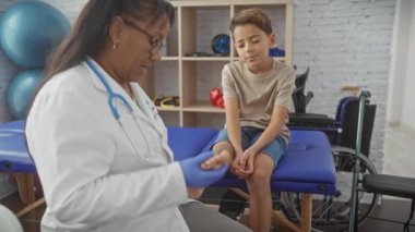 Bir kadın doktor, genç bir erkeğin ayağını modern bir fizyoterapi kliniğinde muayene ediyor..