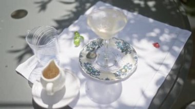 Açık hava kahvaltı masasında güneş ışığında boş bardaklar ve tabaklar, sakin ve doğal gölgede bitirilmiş bir yemeği vurguluyor..